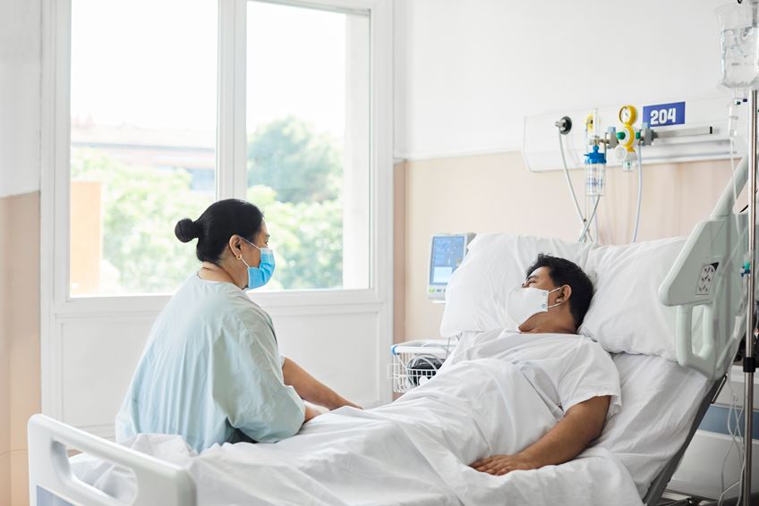 a patient in a hospital bed talking to another person sitting on bed